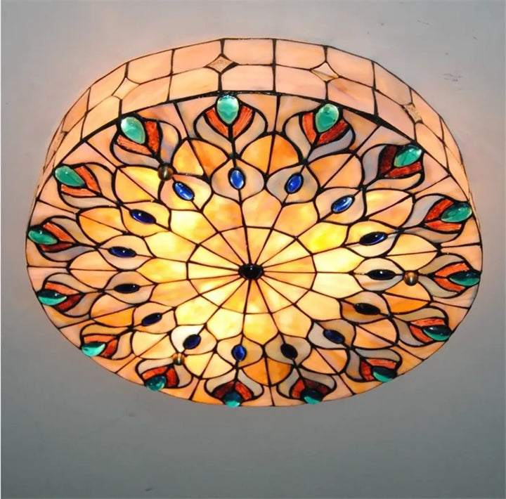 Luminaire plafonnier médiéval circulaire avec motif plume de paon en vitrail aux tons ambre orange et incrustations bleu teal