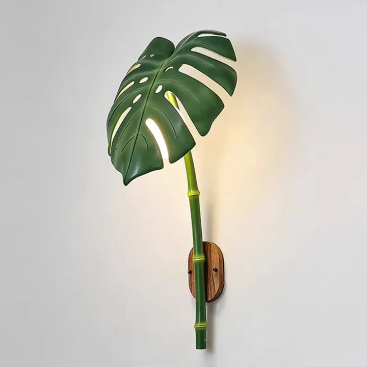 Green monstera leaf wall lamp with bamboo stem and wooden mounting plate for exterior use luminaire extérieur leavah