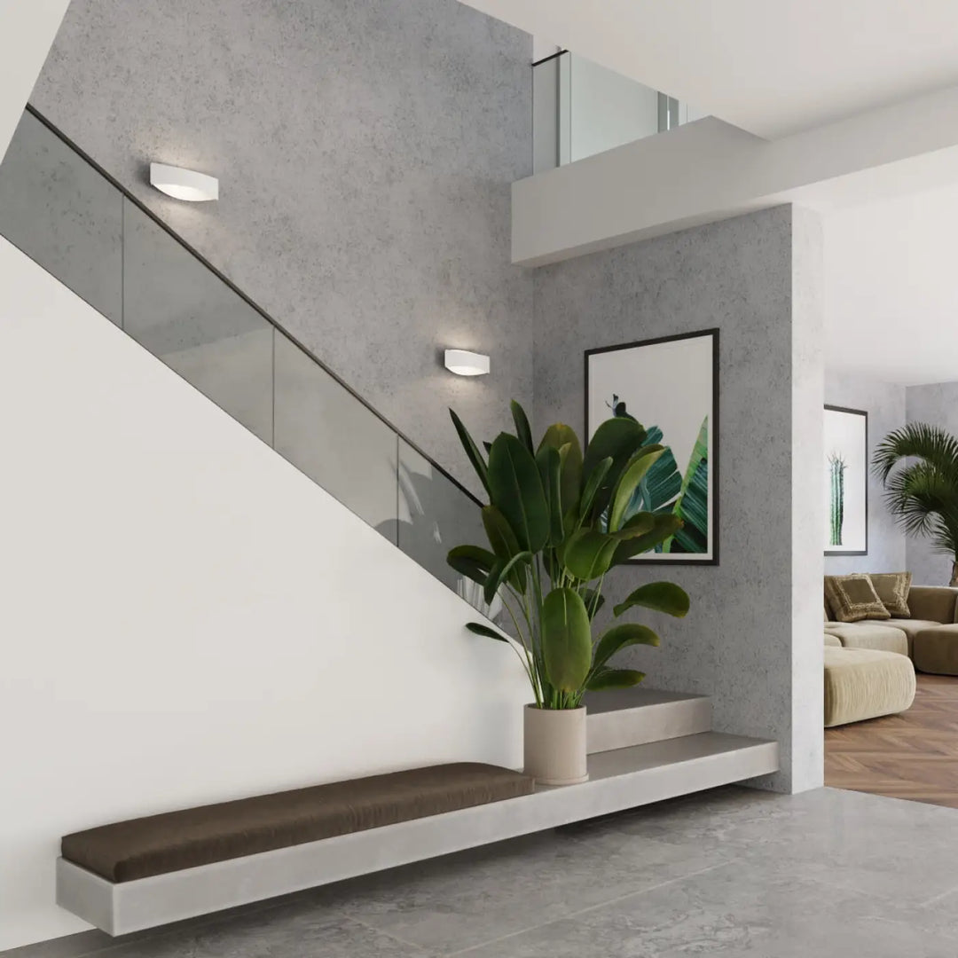 Une applique toni blanc avec une décoration subtile posée près dune plante verte en pot beige sur une étagère flottante