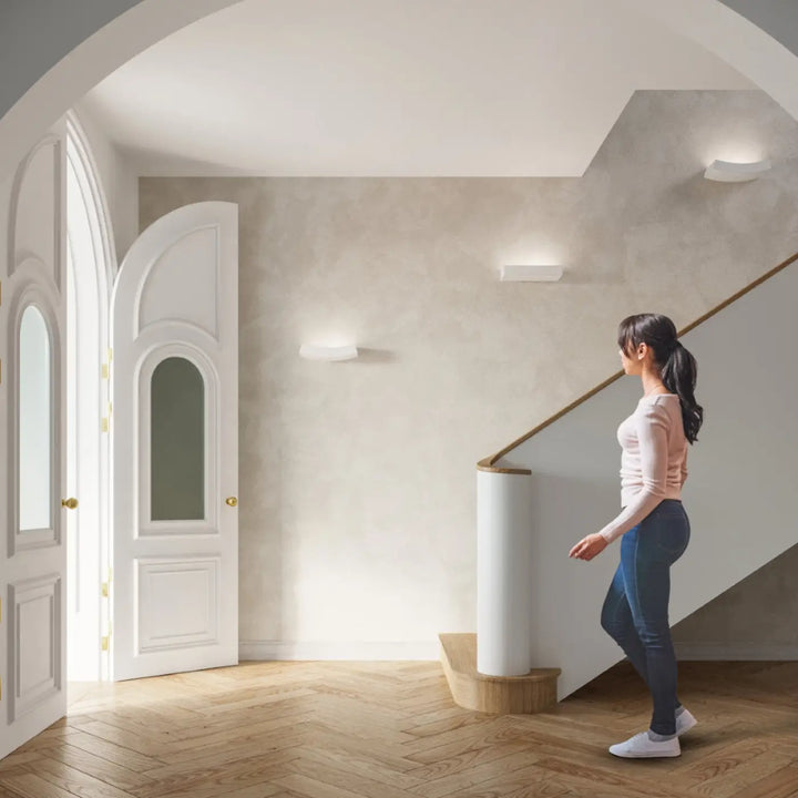 Une femme debout près d’une porte voûtée avec l’applique murale taugan blanc en céramique et plâtre structuré