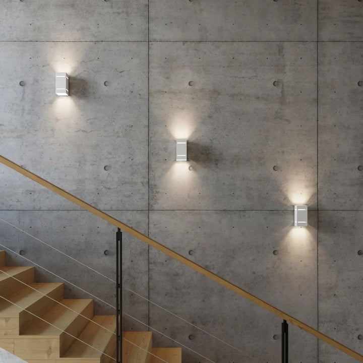 Trois appliques murales blocco blanches minimalistes avec perforation linéaire sur mur en béton pour un spectacle lumineux élégant