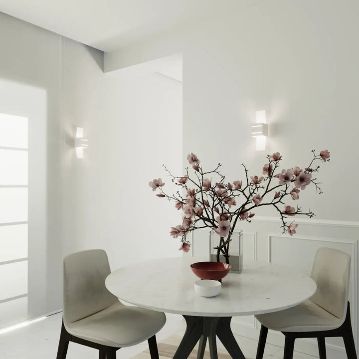 L’applique murale moderne loreto blanc avec perforation linéaire éclaire un spectacle lumineux sur une table en marbre blanc