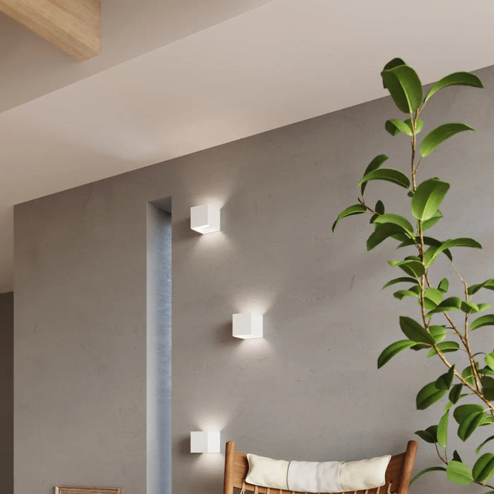 Trois appliques luca carrées blanches en cube minimaliste montées verticalement sur un mur en béton gris avec efficacité énergétique