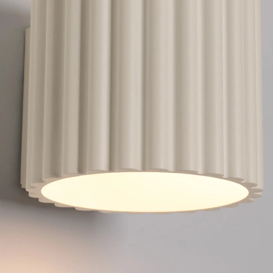 Applique murale beige aura en forme unique inspirée avec structure cylindrique cannelée et lumière circulaire douce à la base
