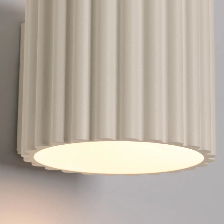 Applique murale beige aura en forme unique inspirée avec structure cylindrique cannelée et lumière circulaire douce à la base
