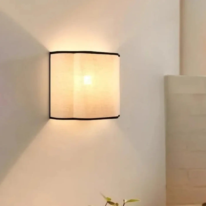 Applique murale carré avec abat-jour beige en tissu et bord noir émettant une lumière douce pour décoration intérieure
