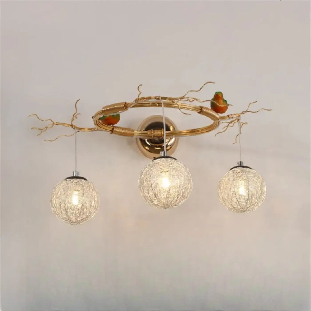 Applique murale moderne sylvana en métal doré avec trois globes en verre tissé et oiseaux décoratifs perchés
