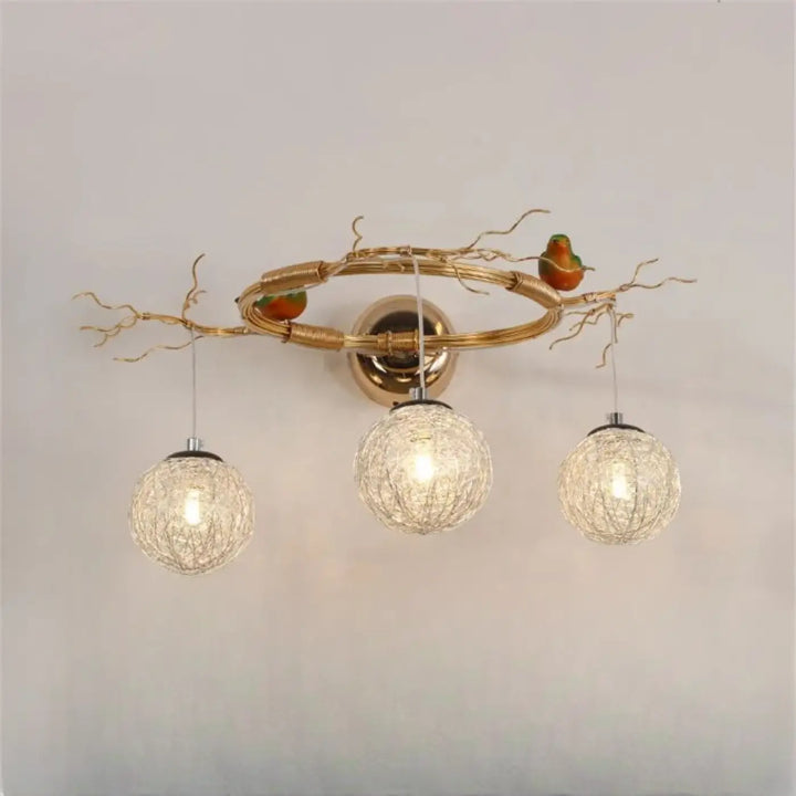 Applique murale moderne sylvana en métal doré avec trois globes en verre tissé et oiseaux décoratifs perchés