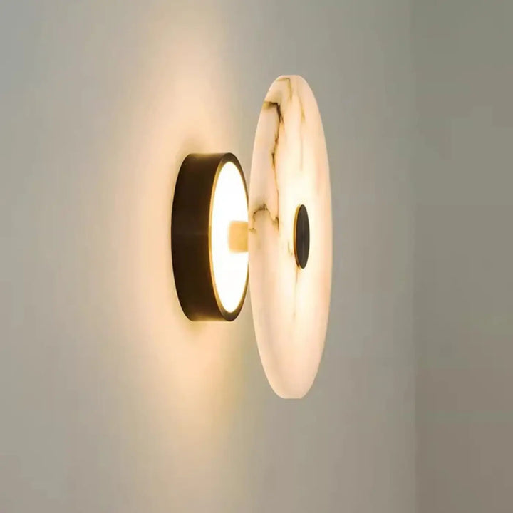 Applique murale moderne moonya avec un disque en marbre beige à veines fines et un support noir émettant une lumière douce