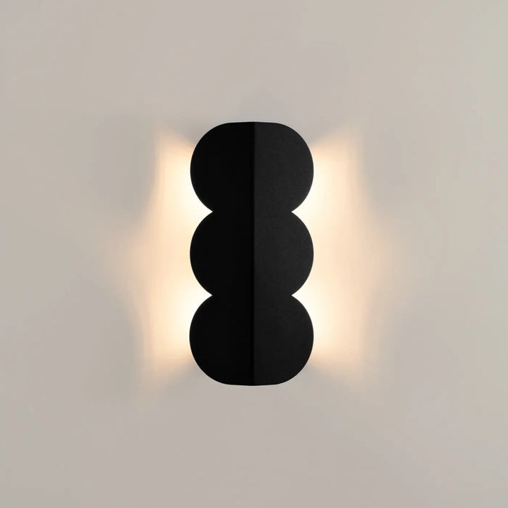 Applique murale biscuit noir avec trois segments circulaires empilés émettant une lumière chaude forme ondulée caractéristique