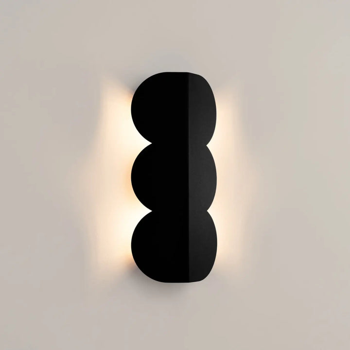 Applique murale biscuit noir avec trois segments circulaires empilés émettant lumière chaude forme ondulée caractéristique