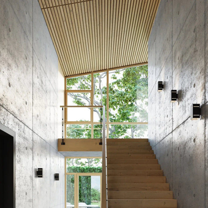L’applique blocco noir avec perforation linéaire éclaire un escalier en bois léger aux murs en béton texturé