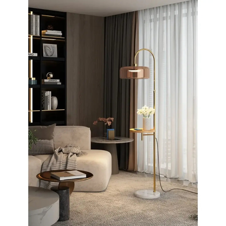 Lampadaire tabora finition moderne doré avec base en marbre, arc courbé, verre ambre et étagère latérale élégante