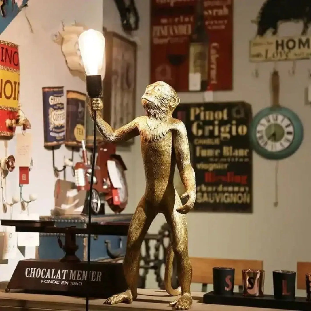 Lampadaire singe golden en métal avec détails fins tenant une ampoule allumée sur une base élégante
