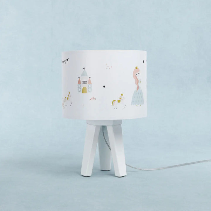 Lampe de table avec abat-jour blanc illustré de princesse féerique et château sur base trépied blanche minimaliste participe à créer une ambiance douce pour chevet blanche