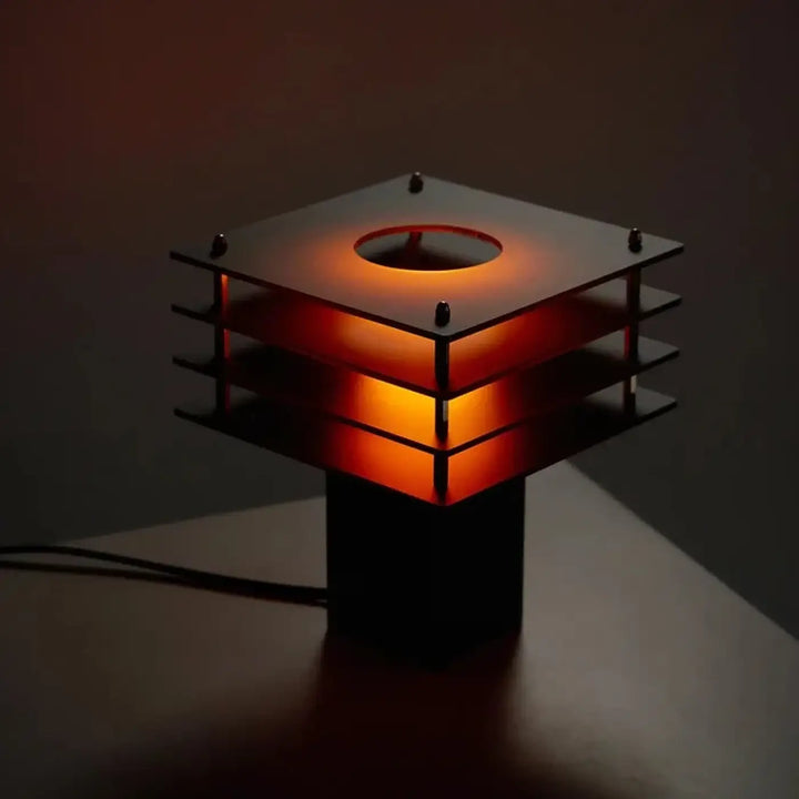 Lampe de chevet sunrise design moderne avec cadre métallique noir et panneaux en verre ambre émettant une lueur douce