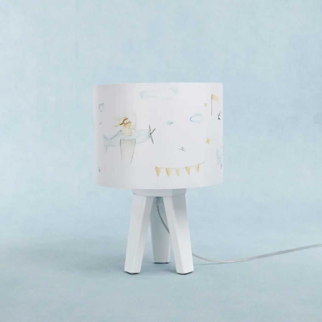 Lampe de table blanche avec abat-jour cylindrique illustré d avions et bannière sur base tripode bleu enfant pour un charmant univers féerique