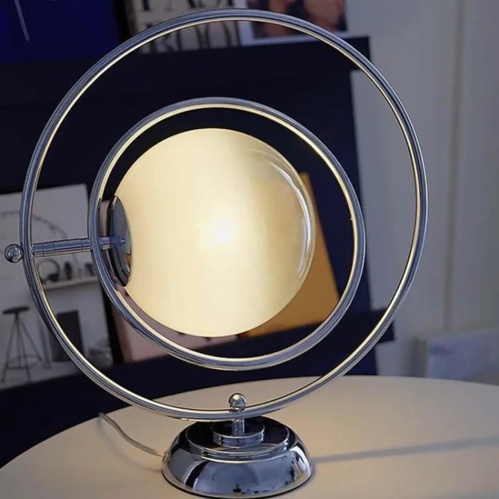 Lampe de table dessi avec base métallique chrome effet planète et ampoule sphérique translucide dans anneaux concentriques