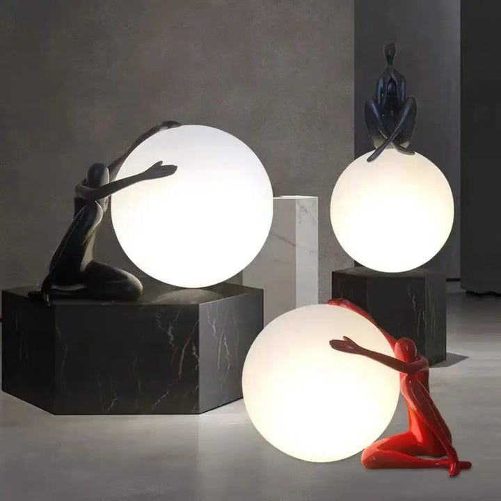 Lampe de table kelya avec trois silhouettes enlacées colorées en noir, rouge et bleu sombre et lumière sphérique sur socles marbre minimalistes