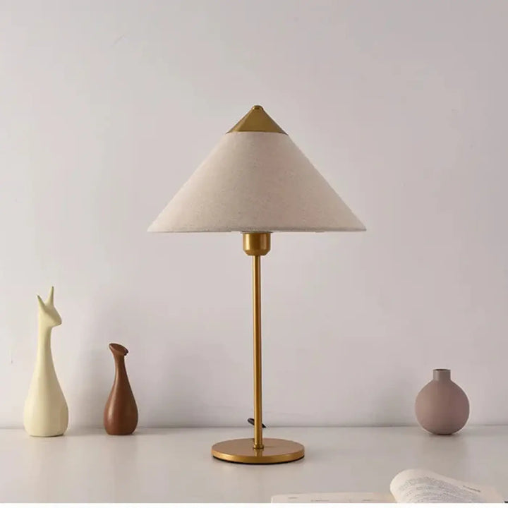 Lampe de table rine avec abat-jour en tissu crème et base fine en métal finition laiton pour une ambiance chic moderne