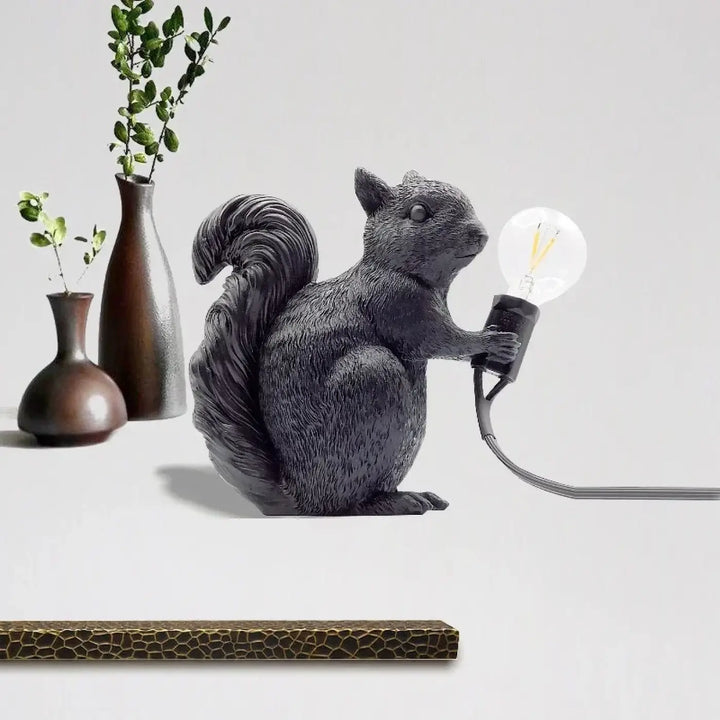 Lampe de table écureuil noire en résine avec surface texturée imitant la fourrure tenant une ampoule edison exposée design écureuil