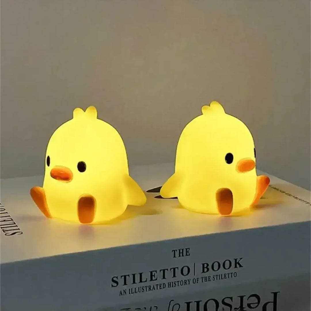 Deux veilleuses canard jaune en silicone avec bouton pile intégré éclairant doucement la nuit posées sur un livre