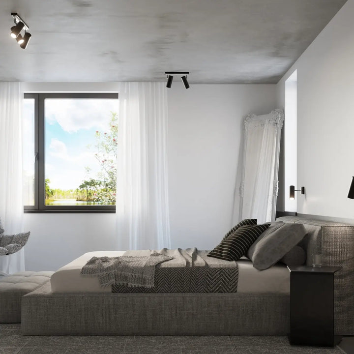 Luminaire plafonnier direzione 3 noir avec éclairage élégant et design plafond minimaliste au-dessus d’un lit plateforme gris en tissu texturé