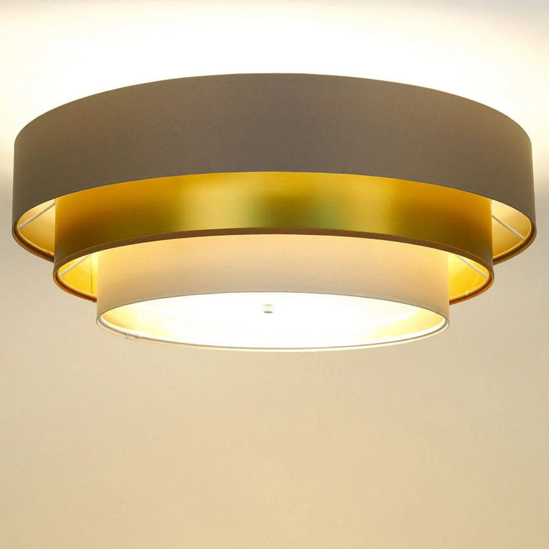 Luminaire plafonnier triniti elegant beige avec design en anneaux métalliques dorés et gris mat émettant une lumière chaude