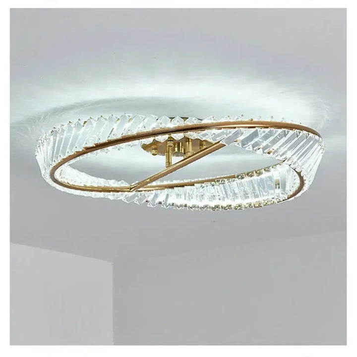 Un plafonnier double anneau moderne avec des montures en métal à teinte dorée et des éléments en cristal transparent, facettés.