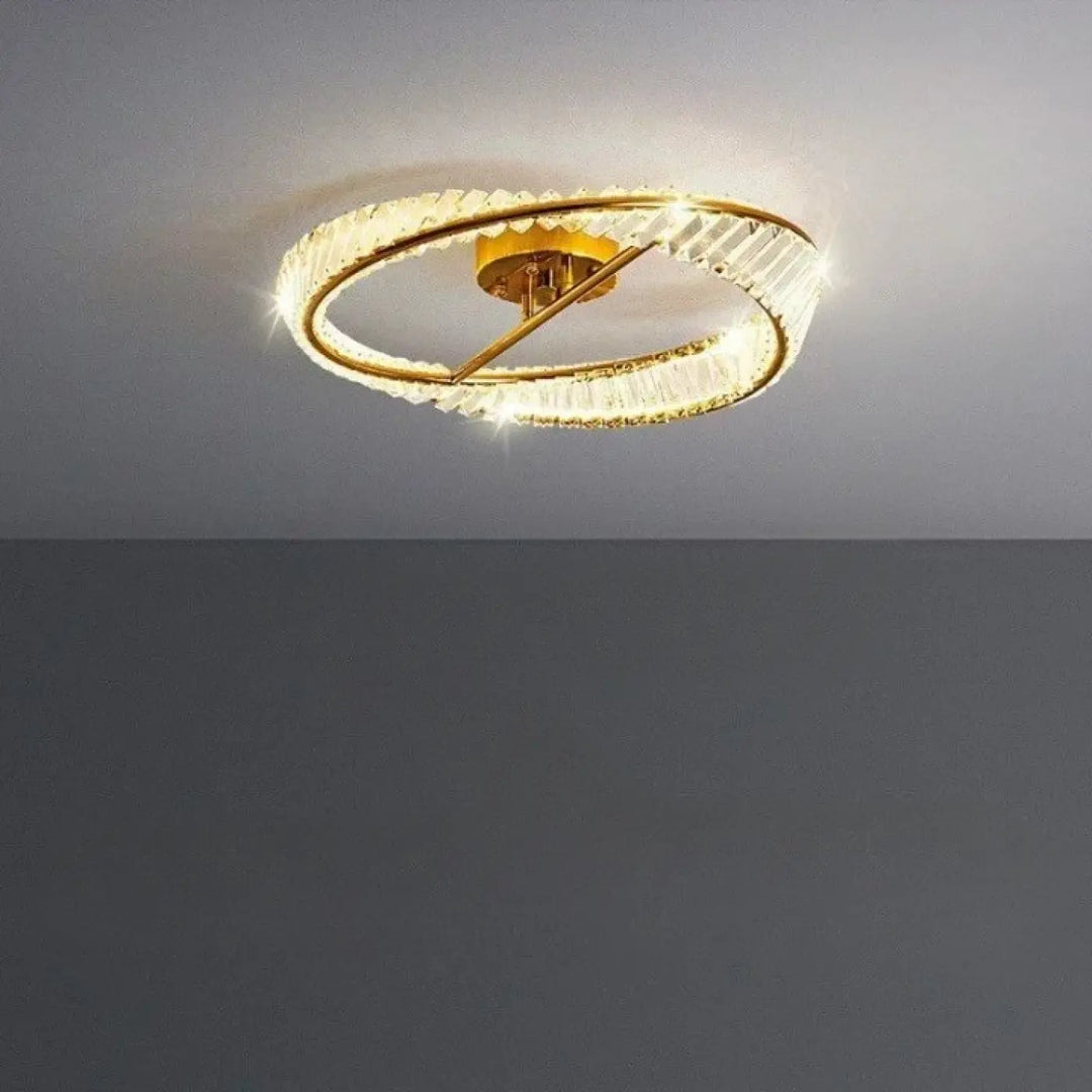 Lustre au plafond à finition dorée, doté de deux anneaux concentriques ornés d’éléments transparents, facettés, façon cristal.