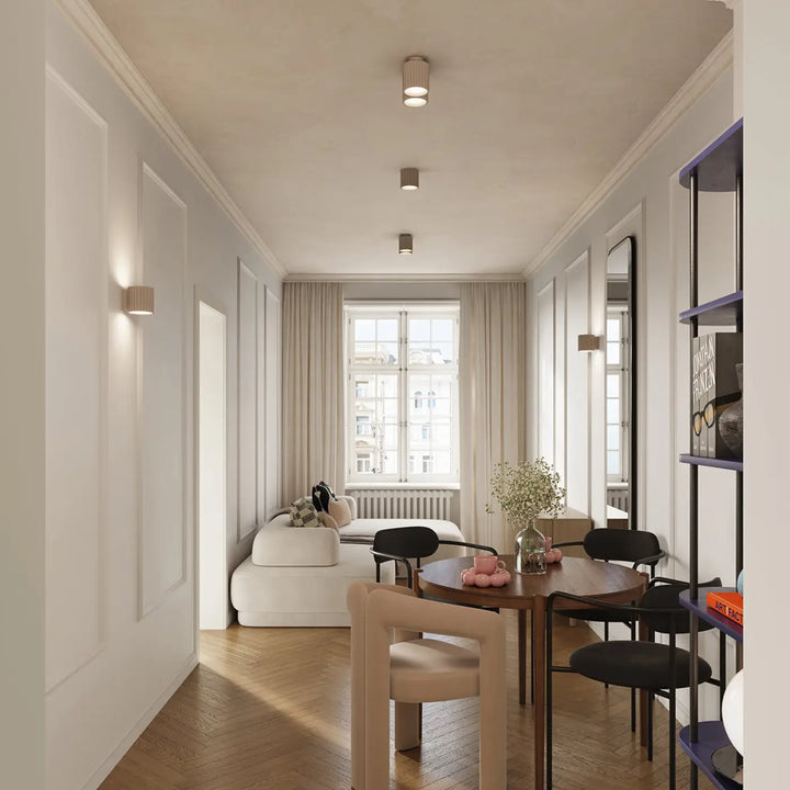 Luminaire plafonnier aura 2 taupe avec forme unique inspirée au-dessus d’une table ronde en bois avec chaises noires et centre décoratif rose