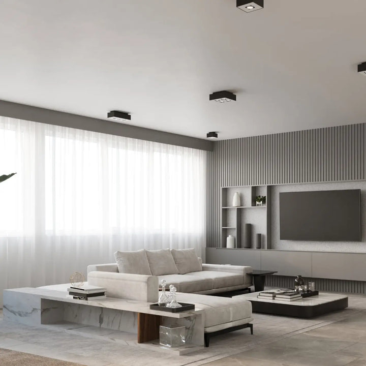 Plafonnier moderne mono noir avec sources lumineuses et spot allongé dans salon minimaliste avec canapé blanc et tables en marbre