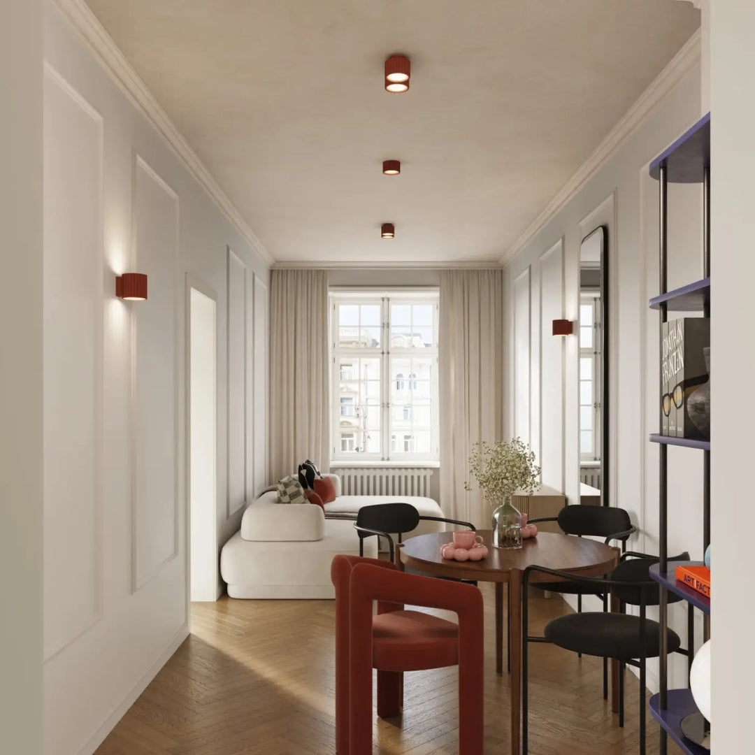 Luminaire plafonnier aura 2 rouge ochra avec forme unique inspirée suspendu au-dessus dune table ronde en bois entourée de chaises noires dont une rouge