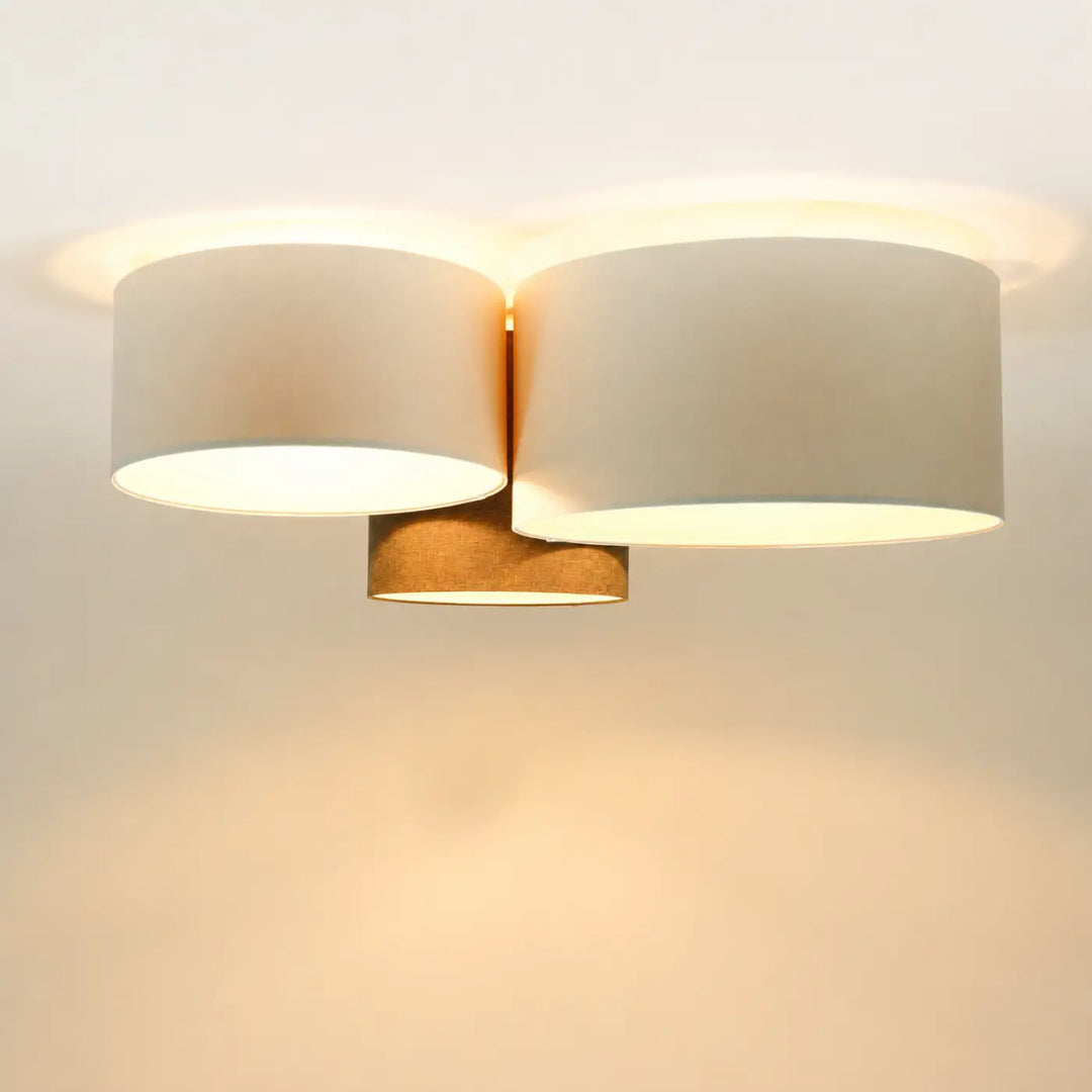 Luminaire plafond moderne avec deux abat-jours cylindriques en tissu beige et base centrale en métal couleur laiton naturel