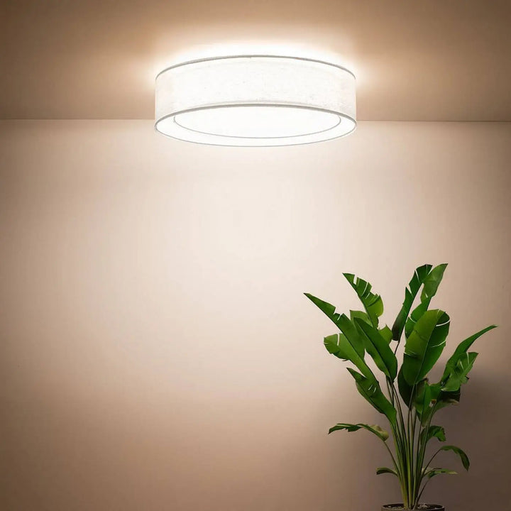 Luminaire plafonnier rond blanc avec abat-jour en tissu blanc et bord métallique émettant une lumière ambiante chaleureuse