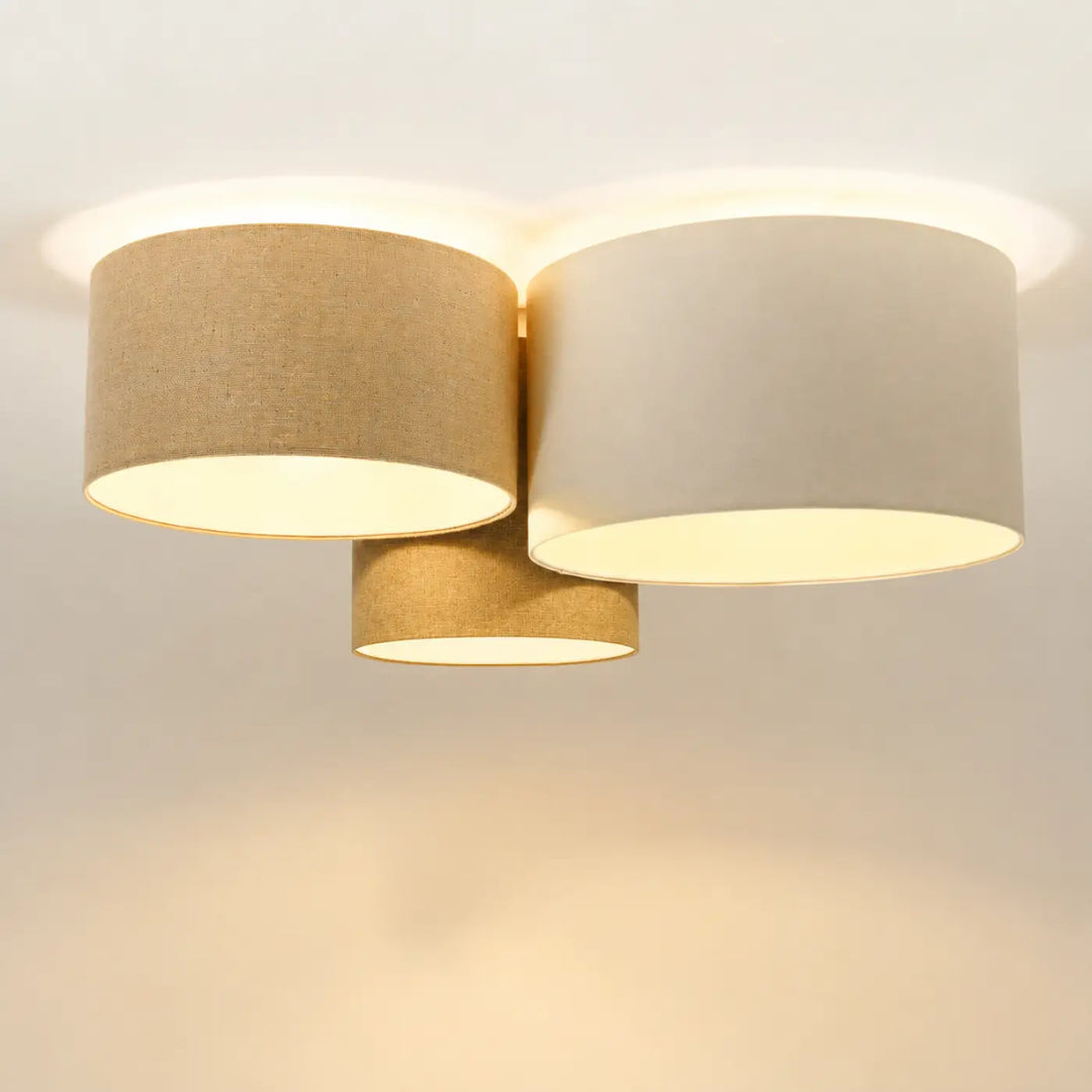 Luminaire plafonnier trio boho elegant avec trois abat-jours cylindriques en tissu naturel beige et crème diffusant une lumière chaleureuse