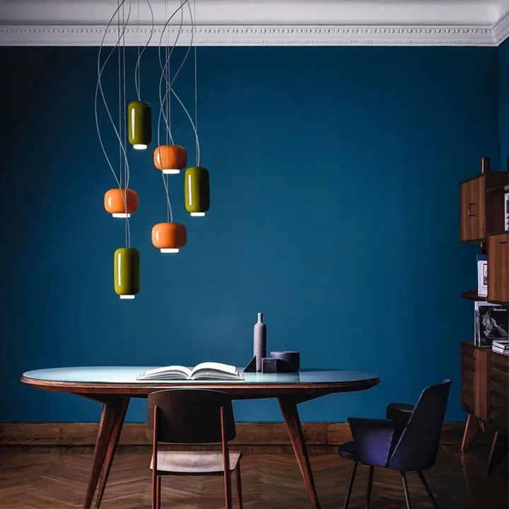 Suspension luminaire moderne aural avec abat-jours cylindriques verts et orange suspendue sur un mur bleu profond
