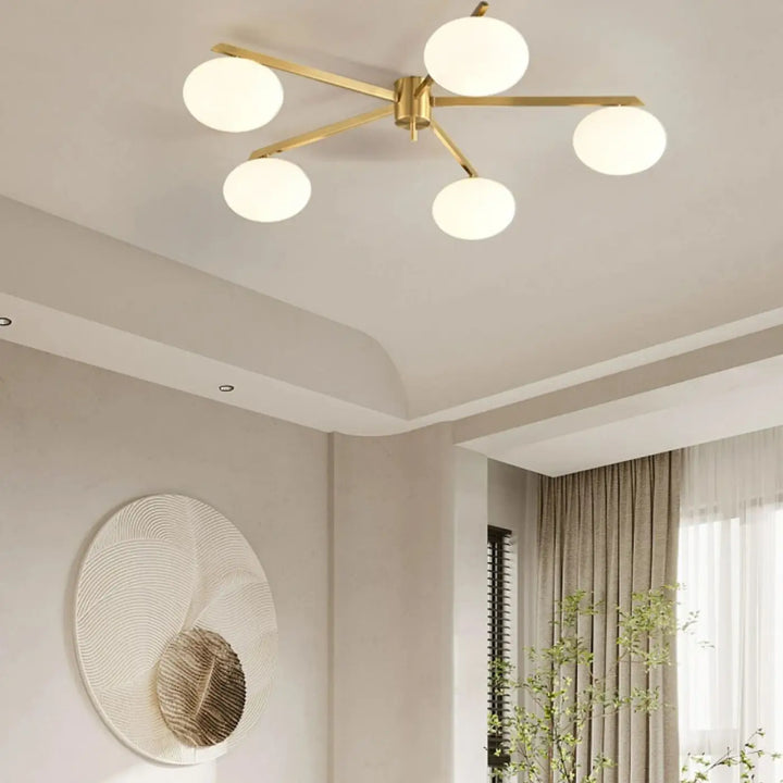 Plafonnier moderne xilys avec cinq globes en verre blanc et bras graphiques dorés ton or