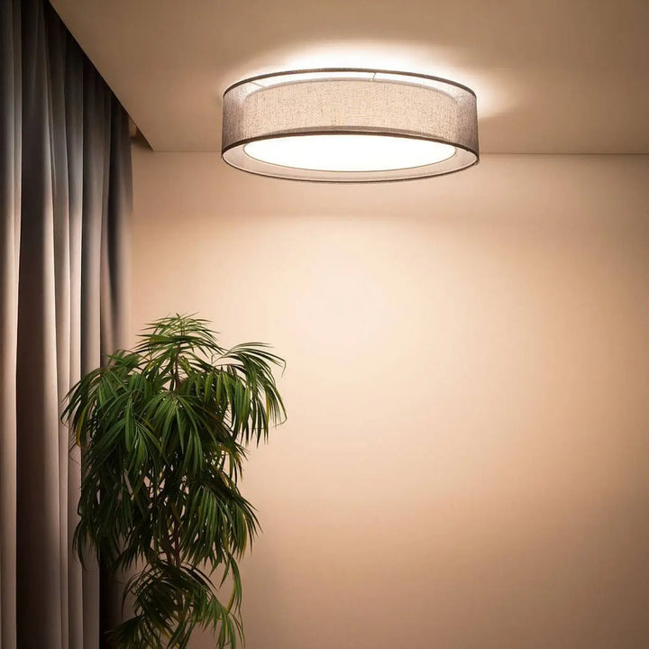 Luminaire plafonnier rond graphite avec abat-jour en tissu gris texturé et bord métallique émettant une lumière blanche chaude