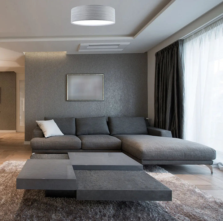 Luminaire plafonnier rond mesh gris en finition textile avec canapé dangle moderne en tissu gris et coussin blanc