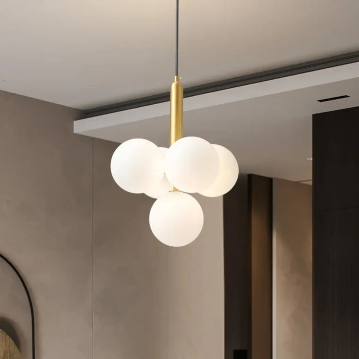 Suspension luminaire dinah avec quatre boules rondes en verre blanc milky white suspendues à une tige métallique dorée