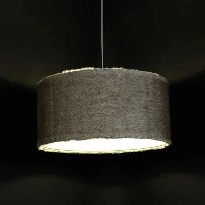 Cylindrique suspension luminaire gris clair avec abat-jour texturé suspendu sur cordon fin contre fond sombre