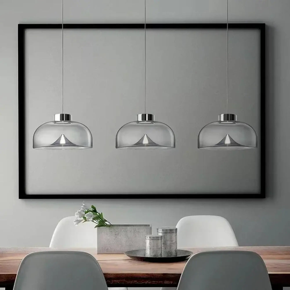 Suspension luminaire eclari avec trois suspensions en verre transparent fumé et fixations métalliques au-dessus d’une table à manger