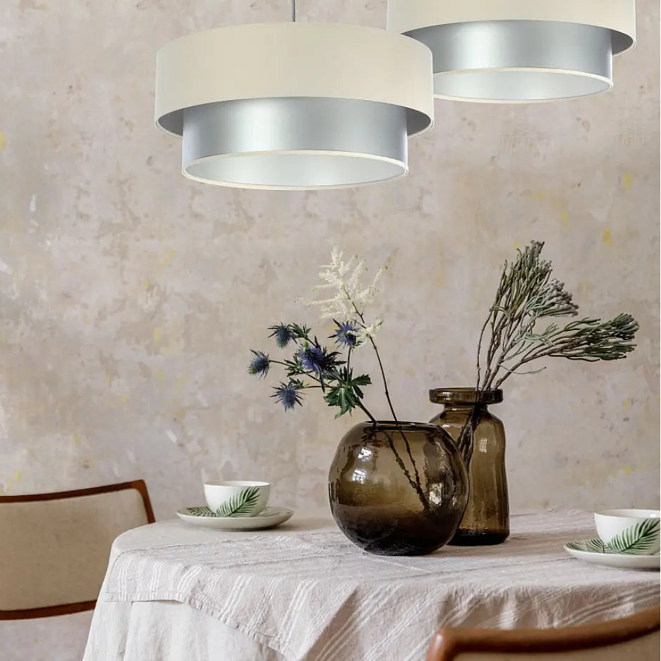 Suspension luminaire duo avec abat-jours cylindriques en crème mat et argent brossé suspendus au-dessus d’une table à manger