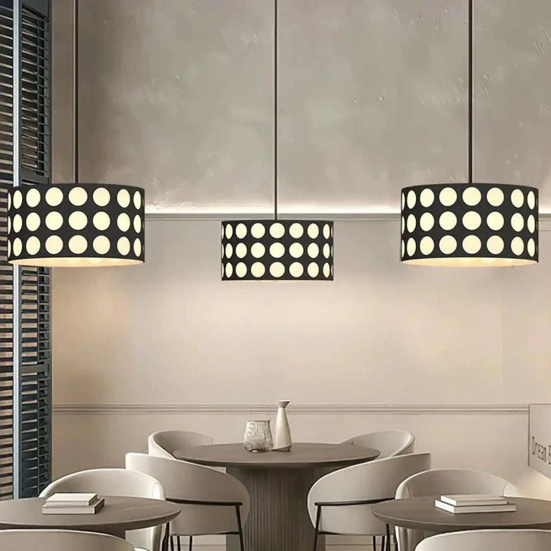 Trois suspensions luminaires cylindriques noires nyxis avec motif de découpes circulaires blanches suspendues au plafond