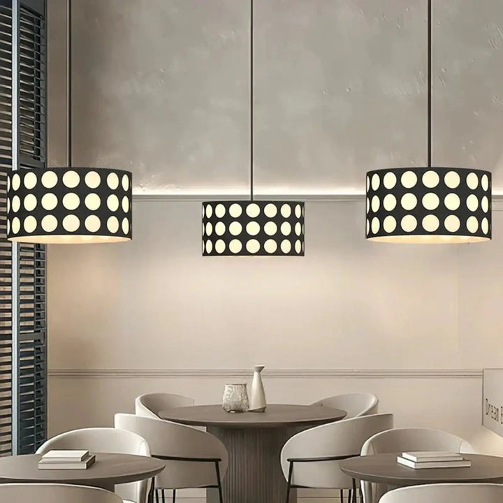 Trois suspensions luminaires cylindriques noires nyxis avec motif de découpes circulaires blanches suspendues au plafond