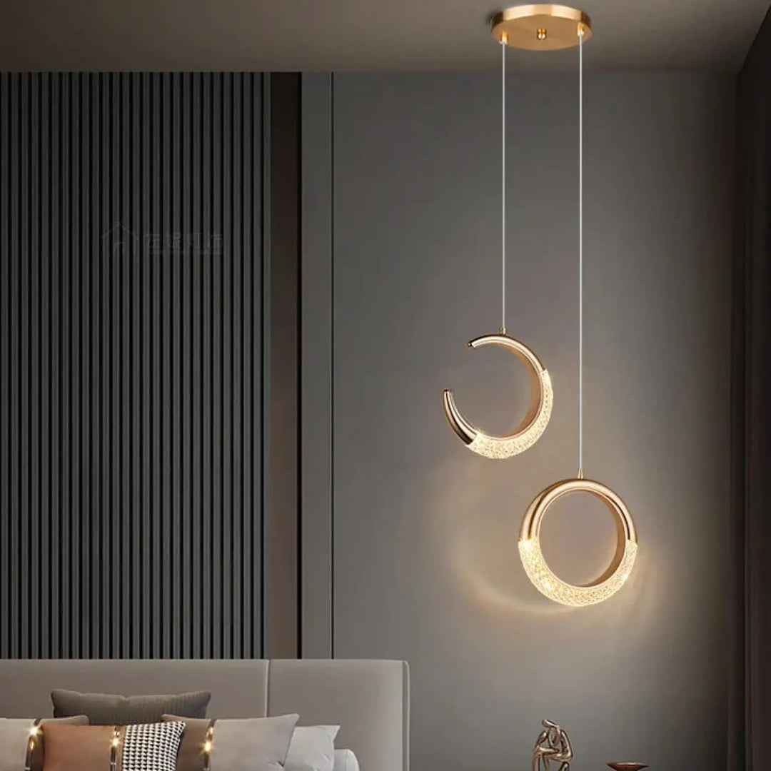 Suspension luminaire aluna en métal doré avec design moderne croissant et cercle, accents en cristal et lumière d’ambiance chaude