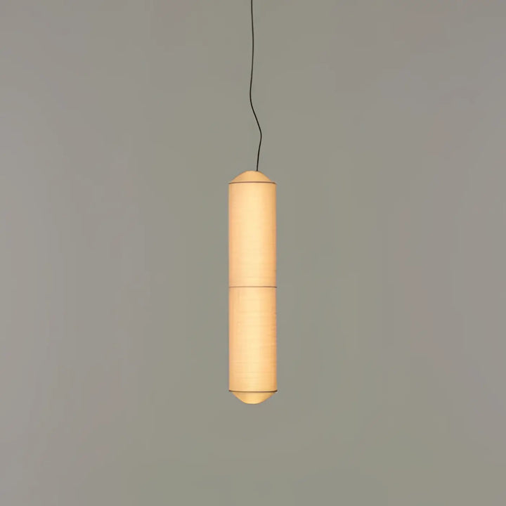 Suspension luminaire papieria en papier cylindrique chaleureux avec lumière douce et ridges verticales au-dessus d’une table