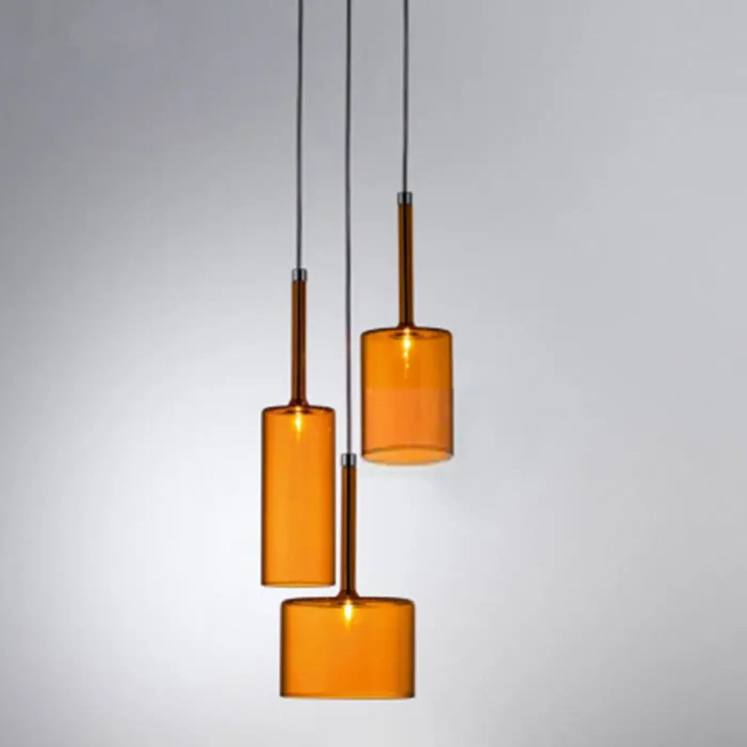 Suspension luminaire cylis avec trois abat jours cylindriques en verre ambré et tiges métalliques élancées suspendues