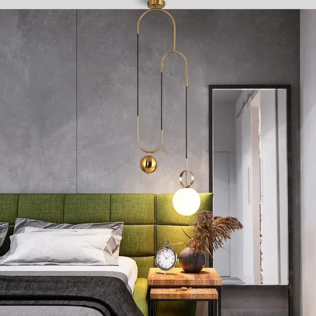 Suspension luminaire pendora dorée avec bras métalliques courbes et globes en verre au-dessus d’un lit vert rembourré